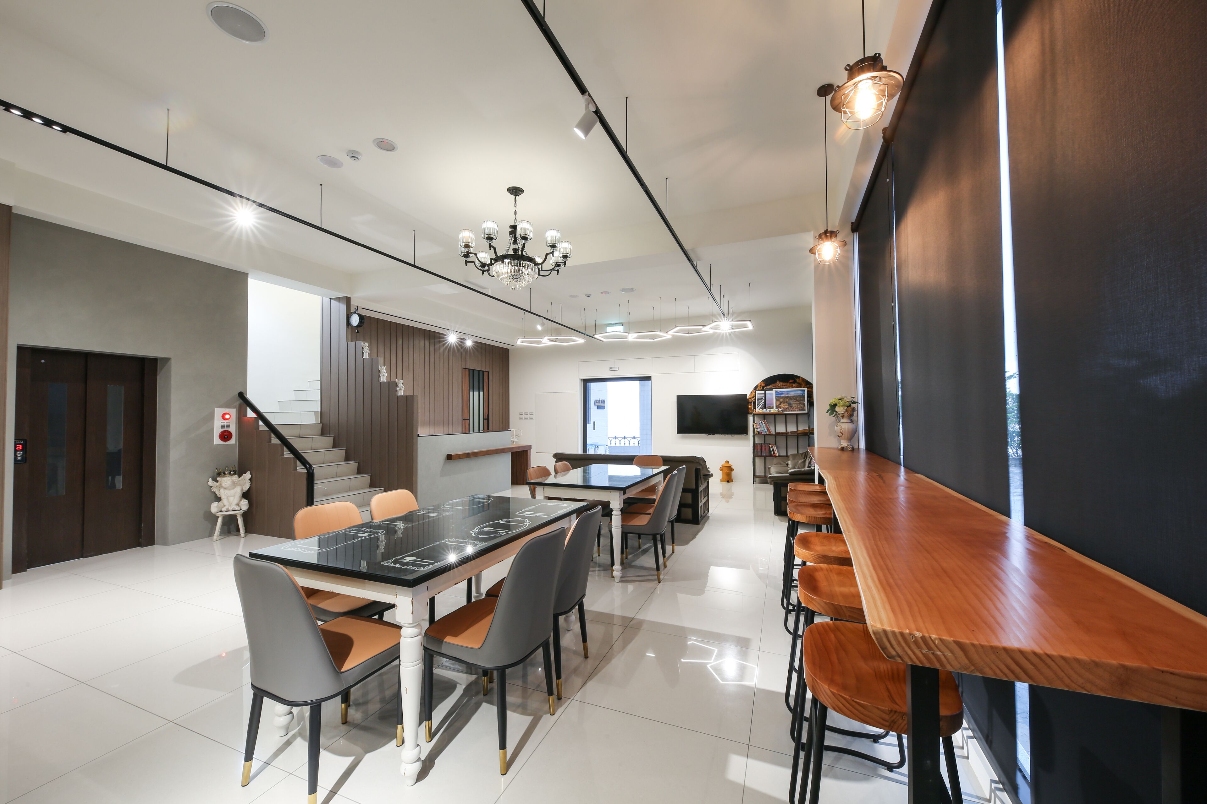 A modern dining area with a long wooden table and chairs, a chandelier, and a staircase leading to an upper level.