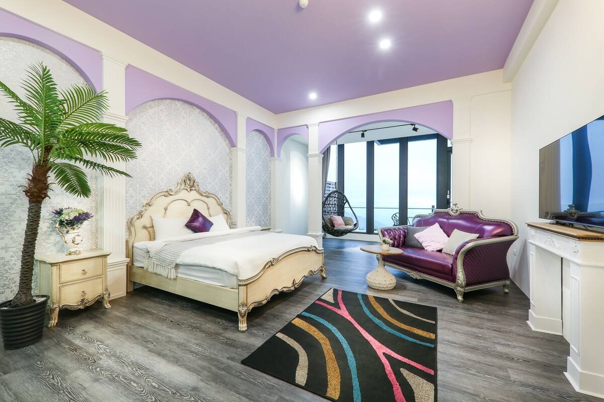 Un dormitorio con cama, sofá, televisor y un ventanal grande.