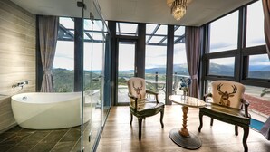 Ein modernes Badezimmer mit einer freistehenden Badewanne, zwei Stühlen mit Hirschmotiven und Blick auf die Landschaft durch große Fenster.