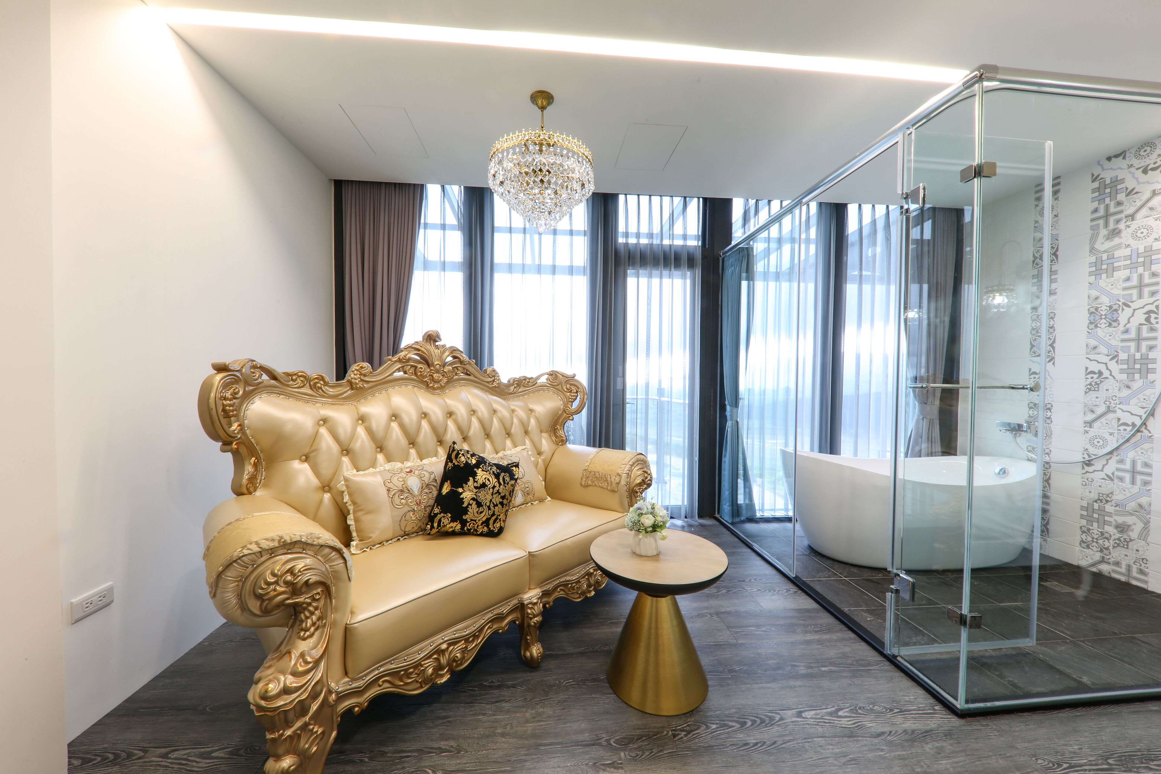 A luxurious room with a tufted gold sofa, a crystal chandelier, and a glass-enclosed shower area.
