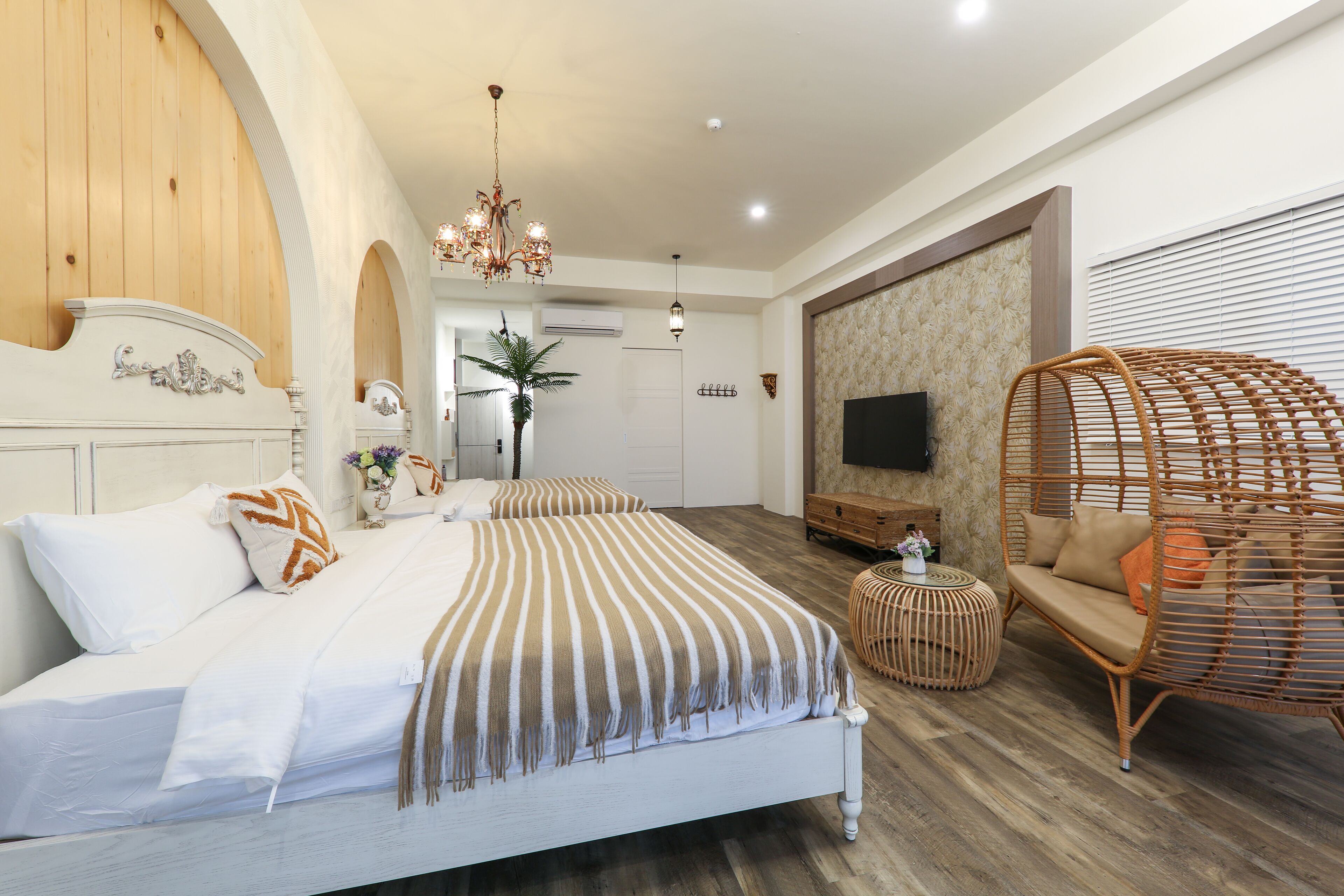 A bedroom with a large bed, a rattan chair, a TV, and a wooden ceiling.