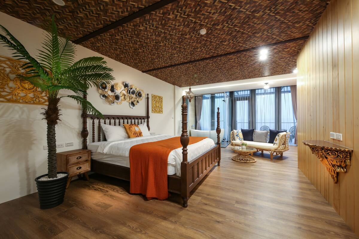 Un dormitorio con una cama de madera, una planta grande en maceta, una mesita de noche, un sofá y un adorno en la pared.