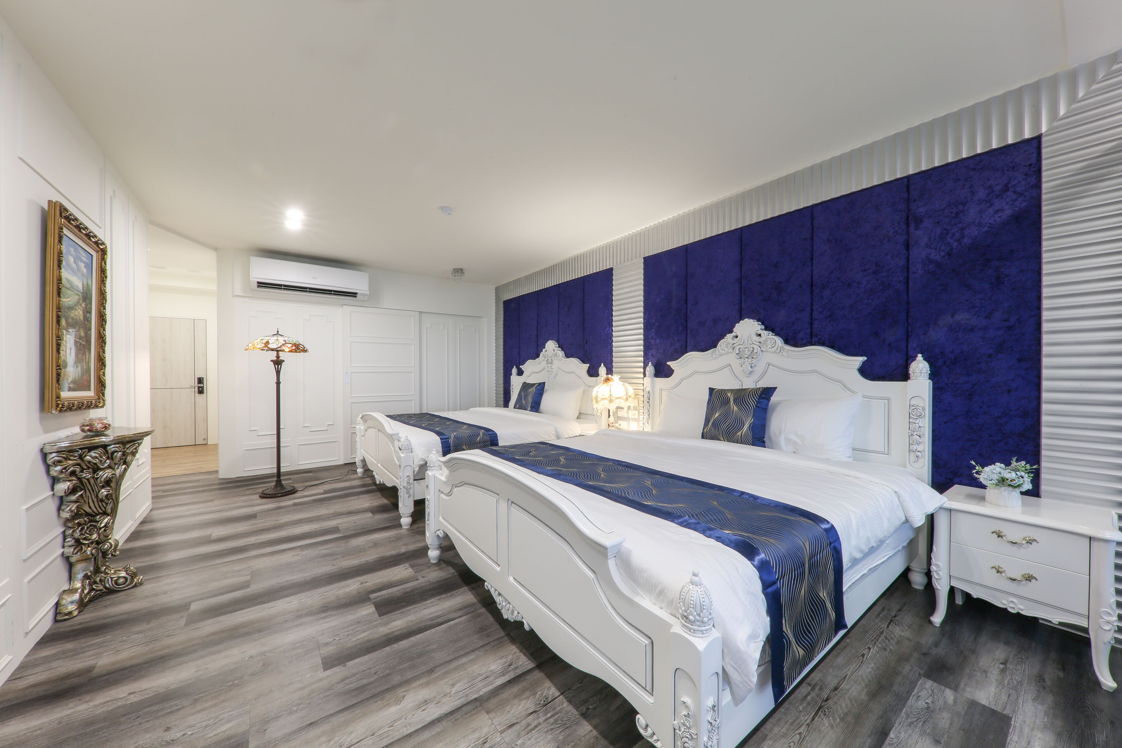 Une chambre avec deux lits, un grand miroir, une lampe sur pied et une commode blanche.