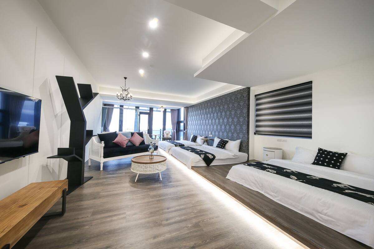 Una habitación de hotel moderna con una cama grande, un sofá, un televisor y un banco de madera.