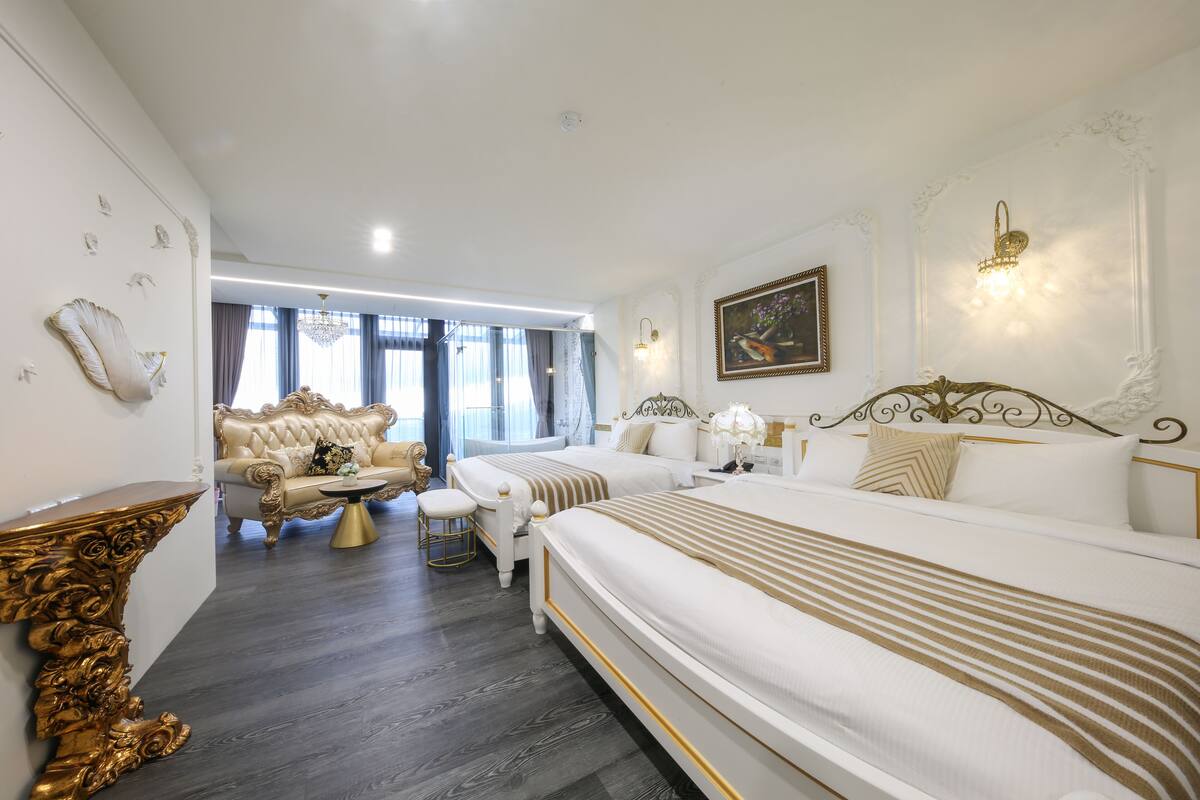 Una habitación de hotel con una cama grande, una zona de estar con un sofá y sillones, y una araña.