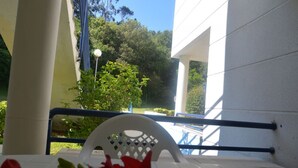 A balcony with a white chair, a pool, and greenery in the background.
