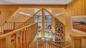 Interior de madera con una escalera, una pared de piedra y vista al exterior.