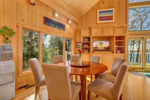 A wooden interior with a dining table, chairs, bookshelves, and artwork.