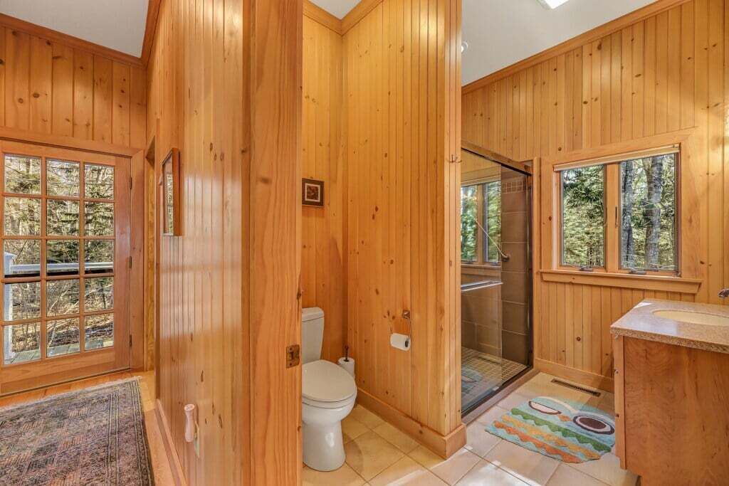 A wooden cabin bathroom with a toilet, shower, and sink.