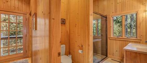 A wooden cabin bathroom with a toilet, shower, and sink.