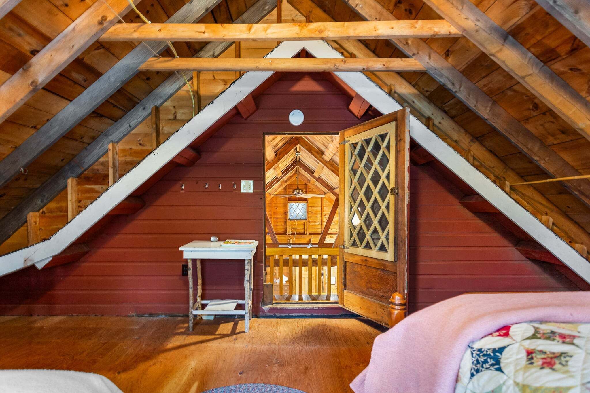 Une chambre mansardée avec un plafond en bois, une petite table et une porte ornée d’un motif en treillis.
