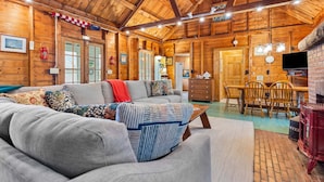 A cozy log cabin interior with a sofa, dining table, chairs, and a fireplace. - Seaside! New-Oceanfront! (Surry)