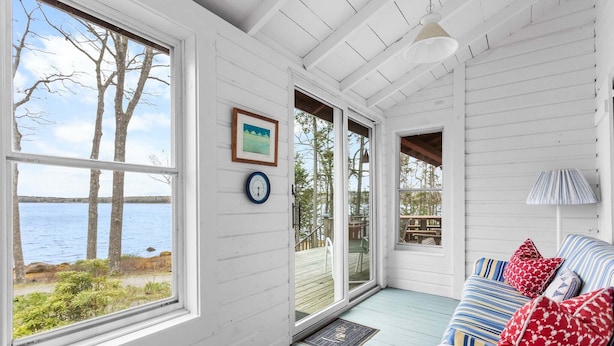 A room with a large window overlooking a body of water, a door leading outside, and a blue-striped sofa with red pillows. - Seaside! New-Oceanfront! (Surry)