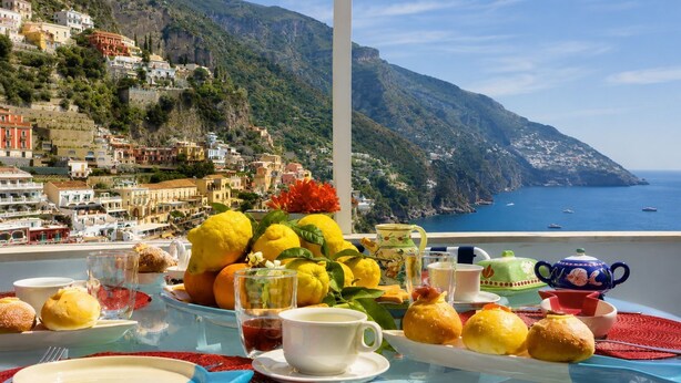 A table set with breakfast items, a view of a coastal town, and a mountainous backdrop. - Villa Positano with sea view (Positano)