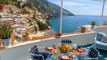 A terrace with a glass table, chairs, and a view of a coastal town.