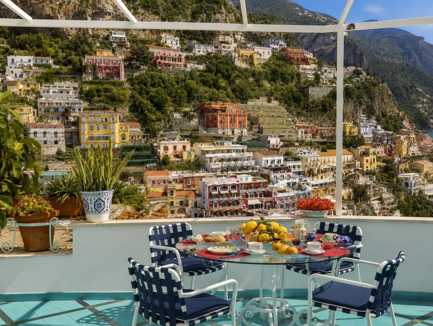 Une terrasse avec une table dressée pour deux personnes, offrant une vue sur un village perché sur une colline, avec ses bâtiments aux couleurs vives.