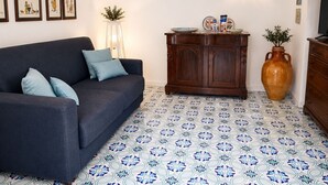 A living room with a dark sofa, a wooden cabinet, a large vase, and patterned floor tiles. - Villa Positano with sea view (Positano)