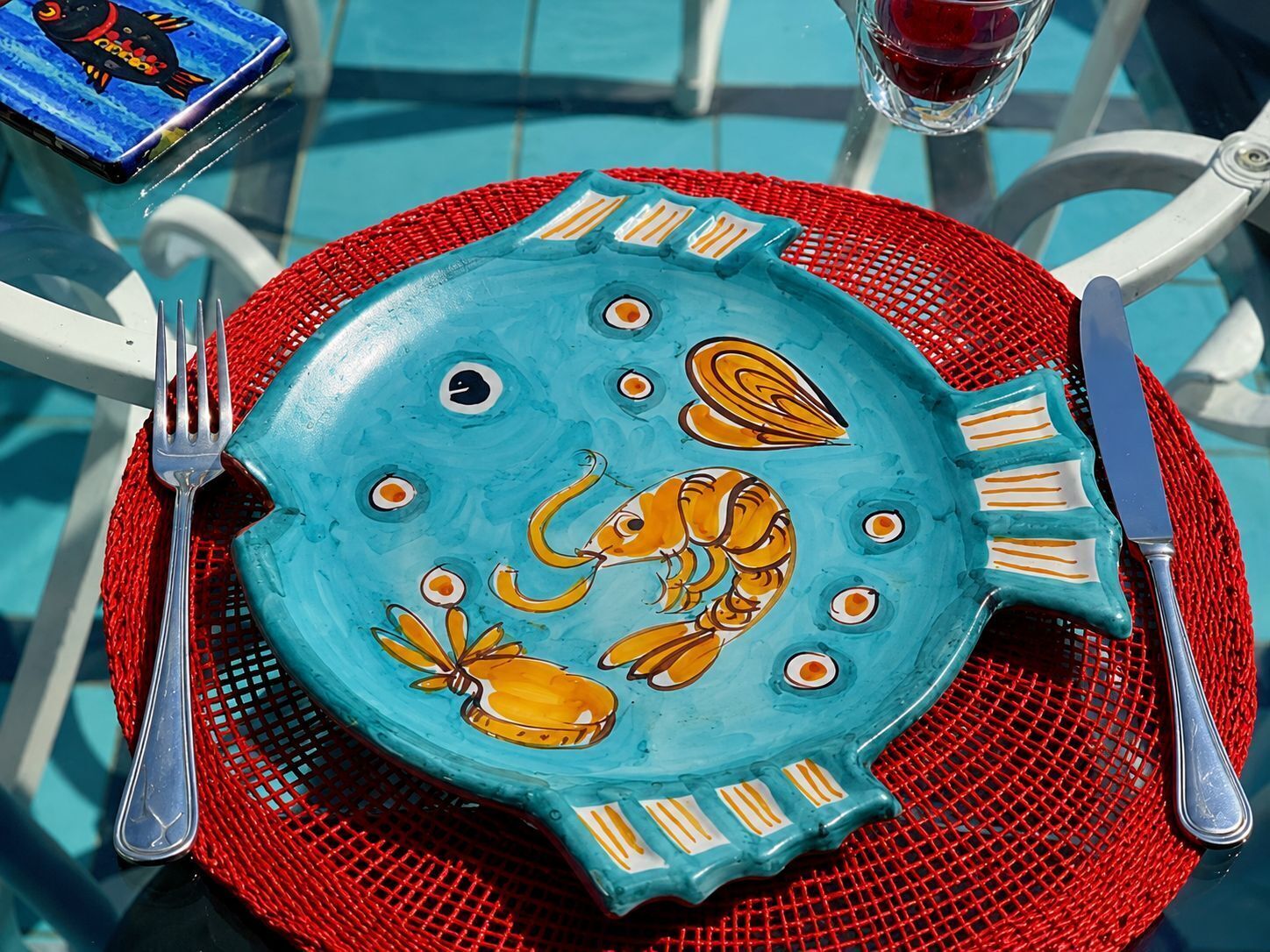 A dining table with a blue plate featuring a lobster design, surrounded by red mesh placemats and silver cutlery.