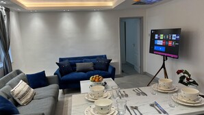 A modern living room with a blue sofa, grey couch, and a dining table set with bowls, glasses, and cutlery. A flat-screen TV is mounted on the wall, displaying various apps. - Luxury 2 Bed Apartment in Royal Sutton Coldfield (Sutton Coldfield)