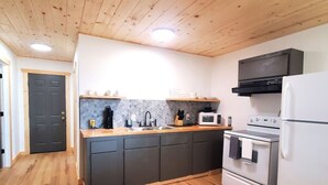 A compact kitchen with a wooden ceiling, a central island with a sink, a microwave, a stove, and a refrigerator.