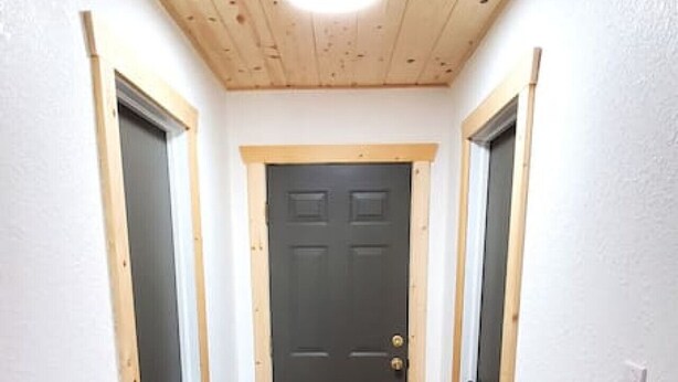 A hallway with wooden flooring, a dark door at the end, and wooden ceiling beams.