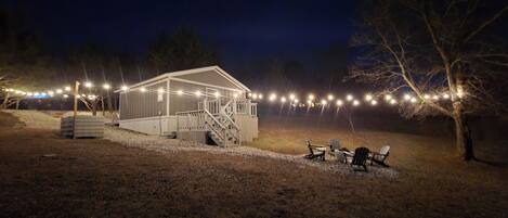 A covered outdoor area with a staircase leading to a building, surrounded by trees and string lights.