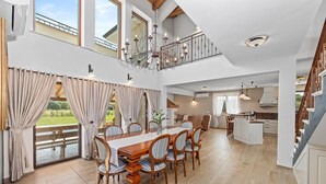 A spacious dining area with a long wooden table and chairs, a staircase leading to an upper level, and a view of a garden through large windows. - Luxury and Stylish Villa Campagna with sauna, private pool and beautiful garden (Pula)