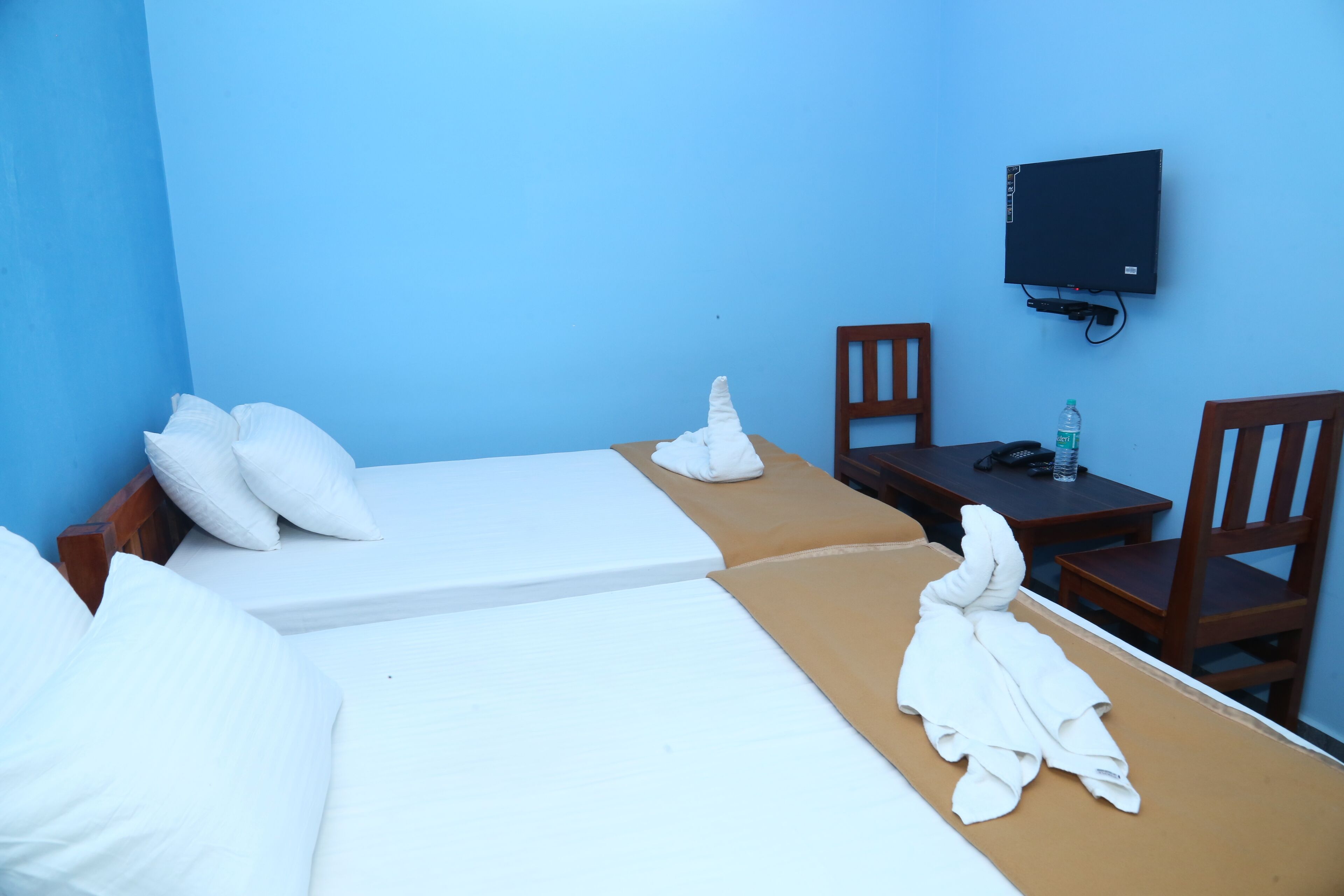 Une chambre d’hôtel avec deux lits, un téléviseur fixé au mur, une table avec des chaises et une bouteille d’eau sur la table.