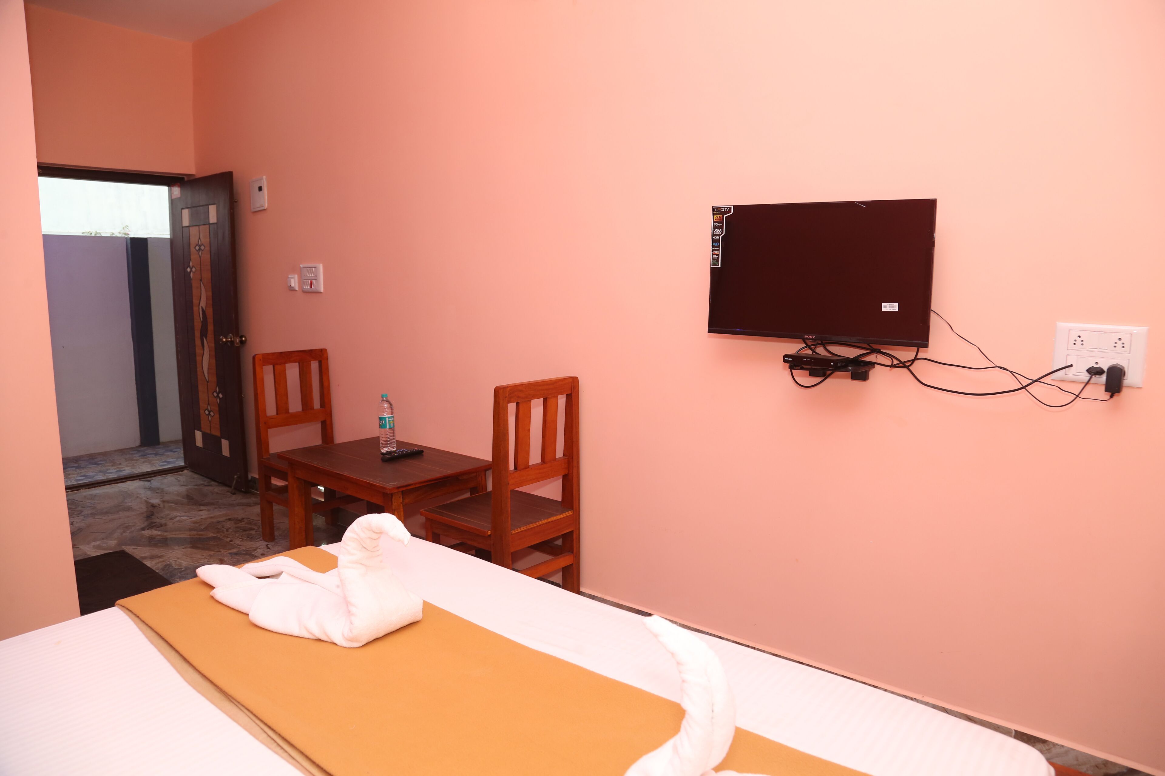 Una habitación de hotel con una cama, una mesa de madera con una silla, un televisor fijado a la pared y una puerta que da a otra habitación.
