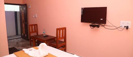 Una habitación de hotel con una cama, una mesa de madera con una silla, un televisor fijado a la pared y una puerta que da a otra habitación.