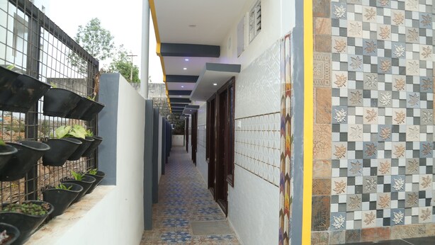 A corridor with a tiled floor, a wall-mounted planter with plants, and a checkered tile pattern on the wall. - Royal Galaxy Inn By Elgozo (Yercaud)