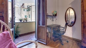 A room with a wooden floor, a desk with a chair, a mirror, and a view of buildings outside. - Central Panoramic Terrace (Florence)