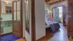 A room with a wooden ceiling, a bed with a patterned bedspread, a window with green shutters, and a view of the outside. - Central Panoramic Terrace (Florence)