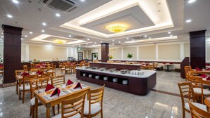 A spacious dining area with multiple tables and chairs, a central buffet station, and a chandelier. - The HUB Hotel (Ho Chi Minh City)
