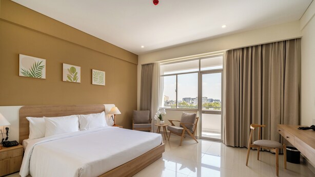 A hotel room with a large bed, a desk, two chairs, a small table with a vase of flowers, and a view of the city through large windows. - The HUB Hotel (Ho Chi Minh City)