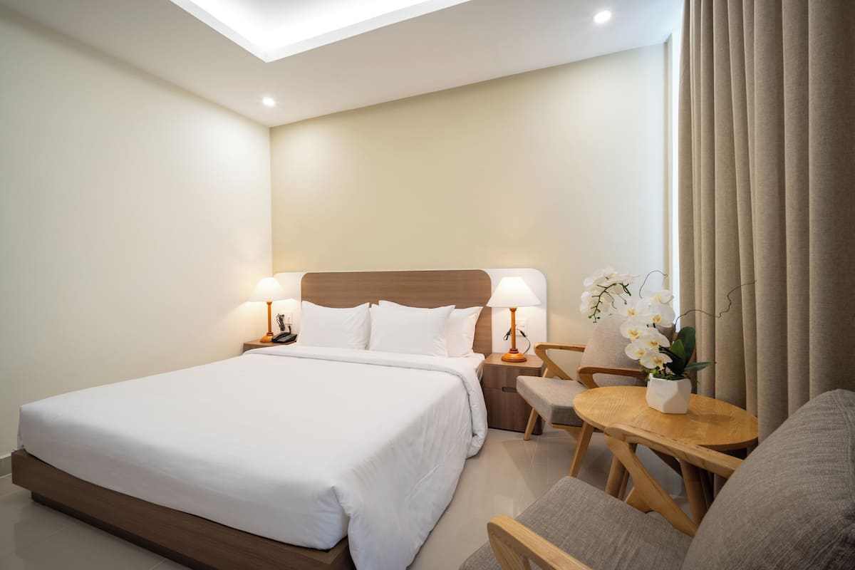 A hotel room with a large bed, bedside tables with lamps, a small round table with a chair, and a potted orchid.
