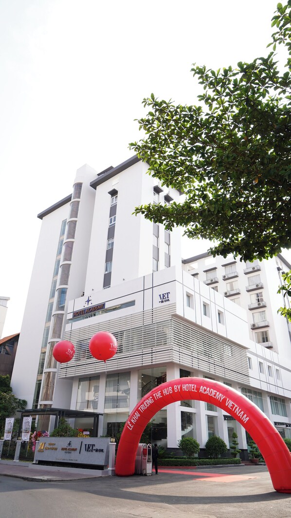 A modern hotel building with a prominent entrance, a large red archway, and a sign indicating it is the Hotel Academy Vietnam. - The HUB Hotel (Ho Chi Minh City)