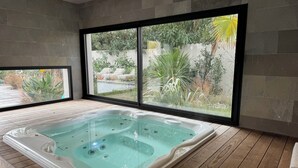 A modern bathroom with a large bathtub, wooden flooring, and a view of a garden through large windows. - Luxury villa heated pool jacuzzi sauna (Pérols)