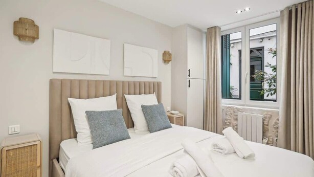 Una habitación de hotel moderna con una cama grande, dos lámparas fijadas a la pared y un ventanal con cortinas.
