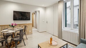 Una sala de estar moderna con comedor, un ventanal con cortinas y un televisor de pantalla plana montado en la pared.