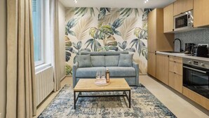 Una sala de estar moderna con un sofá, una mesa de centro y una zona de cocina con armarios y electrodomésticos.