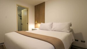 Una habitación de hotel con una cama grande, una mesita de noche con lámpara y un panel de madera en la pared.