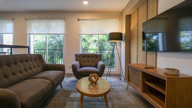 Una sala de estar con sofá, sillón, mesa de centro redonda y televisor sobre un mueble de madera.