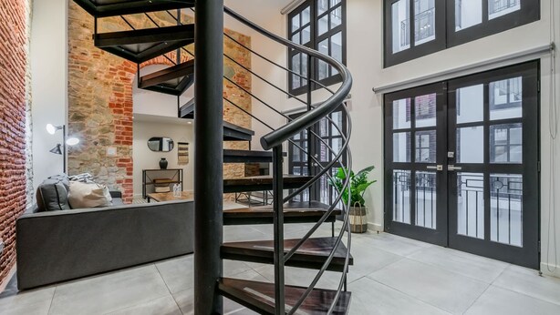Un intérieur moderne avec un escalier en colimaçon, un mur en briques et de grandes fenêtres.