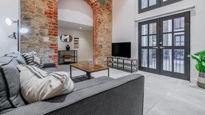 Un salon moderne avec une arche en pierre, un canapé gris, une table basse en bois et un téléviseur à écran plat.