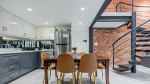 Une cuisine moderne avec des meubles gris, un réfrigérateur en acier inoxydable et un coin repas comprenant une table en bois et des chaises marron.