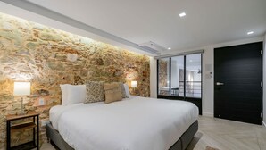 Camera da letto con parete in pietra, letto con biancheria bianca, due lampade da comodino e una porta nera.