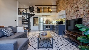 Un soggiorno moderno con una scala che conduce a una mansarda, una cucina con elettrodomestici in acciaio inossidabile e una grande televisione a schermo piatto.