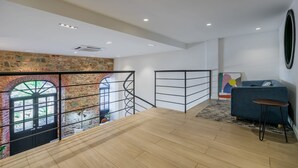 Un'ampia stanza con pavimento in legno, un divano blu, un piccolo tavolino rotondo e un grande quadro astratto appeso al muro.