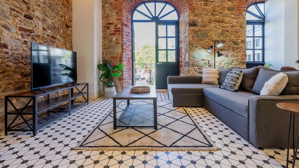 Un soggiorno con una parete in pietra, una TV su un mobile, un divano e un tappeto decorato.
